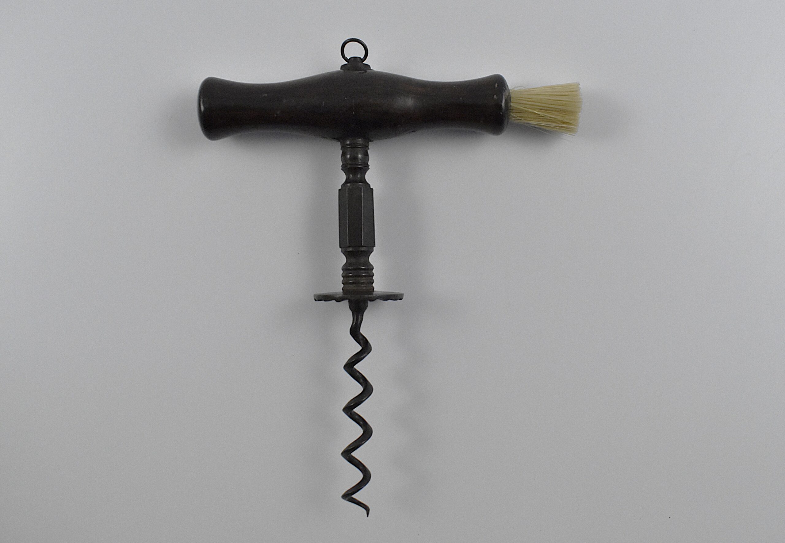 An English straight pull corkscrew with wood handle incorporating a dusting brush and hanging ring. Turned and faceted steel stem ending in a ‘Henshall button’, the underside of which is cut with fluting.