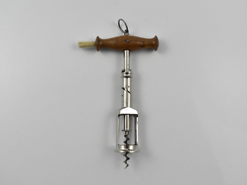 A German chrome plated steel open frame corkscrew with turned wood handle incorporating a dusting brush and hanging ring. The handle is turned into the cork and when the two pins in the shaft engage the top of the second shaft, this reverses and extracts the cork from the bottle. This design originates from the 1880 German patent taken out by Freidrich Kummer and later adapted by his son Louis Kummer. Perfect centre cut bladed worm.